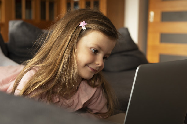 漂亮的女孩在笔记本电脑上看动画片。图片下载