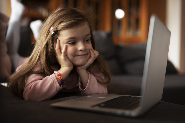 漂亮的女孩在笔记本电脑上看动画片。图片下载