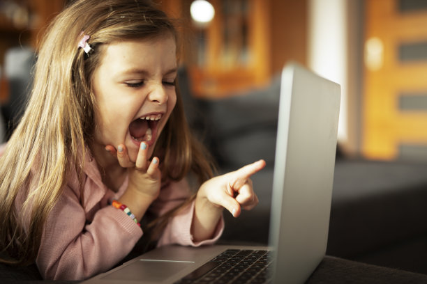 漂亮的女孩在笔记本电脑上看动画片。图片下载