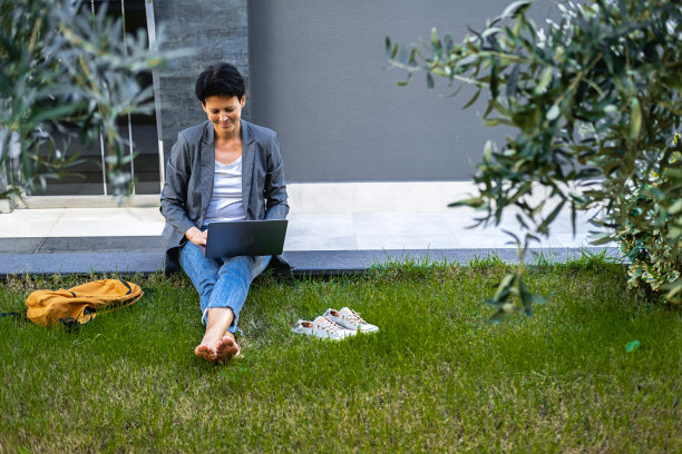 一个女人坐在草地上，拿着一台笔记本电脑，看着小工具的屏幕。图片下载