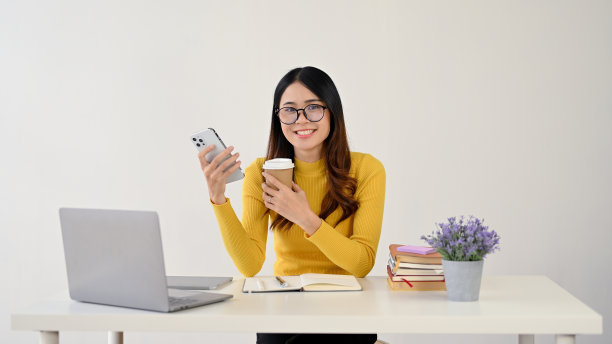 一个迷人的亚洲女大学生坐在她的办公桌前。孤立在白色背景上图片下载