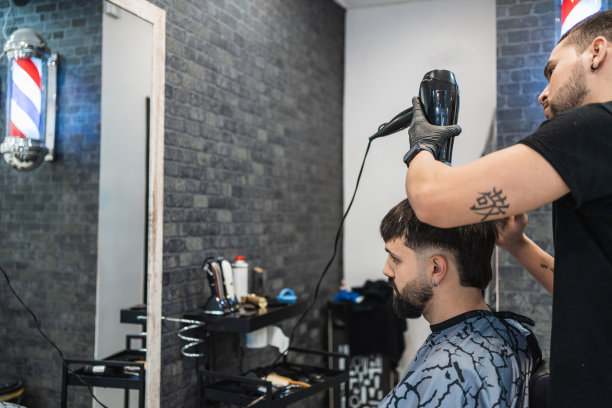 理发师一边照镜子，一边用吹风机吹干客户刚处理过的头发。图片下载