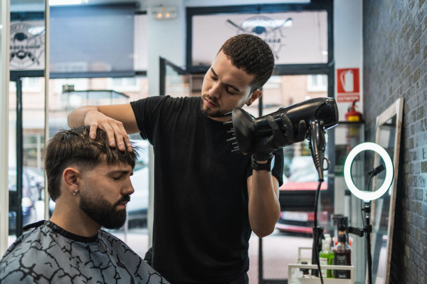 理发师正在用吹风机吹干客户刚处理过的头发。图片下载