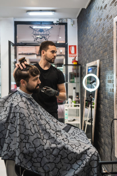 理发师看着镜子的同时，他的客户谈论他将在理发店剪的头发。图片下载