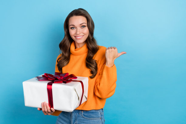照片中可爱有趣的女士穿着针织套头衫拿着礼物盒拇指空白的空间孤立的蓝色背景图片下载