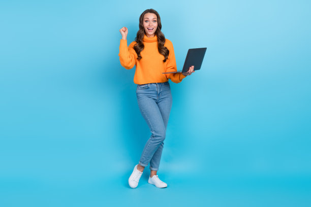 兴奋的幸运女士穿着橙色套衫赢得游戏的全长照片现代设备孤立的蓝色背景图片下载