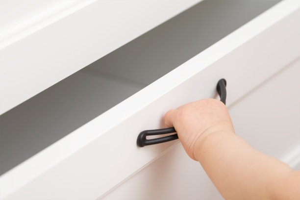 婴儿手握把手，打开或关闭白色抽屉在家里的房间。特写镜头。侧视图。图片下载