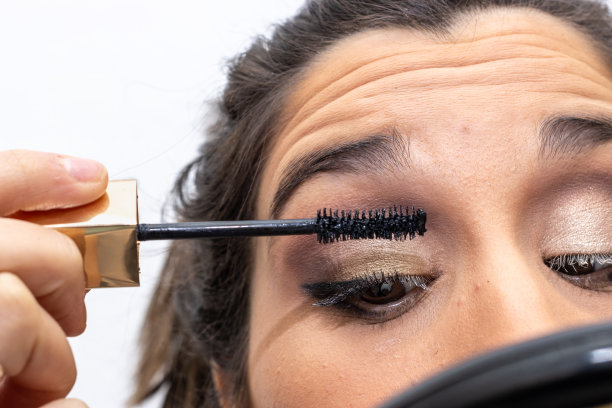 女孩拿着彩妆笔看着手里的镜子。迷人的自然女孩拿着镜子画眼线图片下载