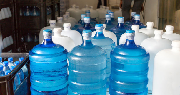 塑料大瓶或白色和蓝色加仑的纯净饮用水在生产线内准备销售。饮水厂，小本经营图片下载