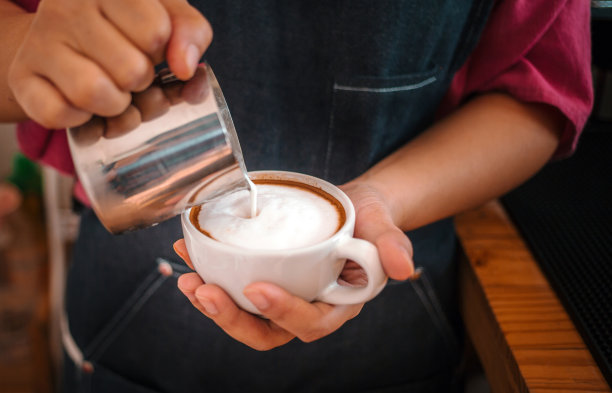 咖啡师在制作卡布奇诺时往咖啡里加牛奶。咖啡师制作卡布奇诺，专业调酒师准备咖啡饮品图片下载