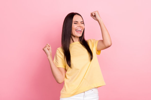 照片中，高兴的女士举起拳头赢得彩票头奖，尖叫着喜出望外，穿着黄色衬衫，孤立的粉红色背景图片下载