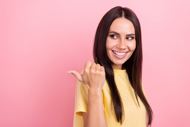 照片的梦幻光泽的女人穿着黄色t恤，看起来显示拇指背面空白空间孤立的粉红色背景图片下载