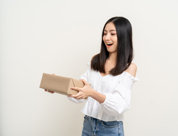 年轻、兴奋、美丽的亚洲女人拿着包裹纸板站在孤立的背景上。兴高采烈的女士拿着一大堆包裹箱，从快递公司收到网上购物的申请图片下载