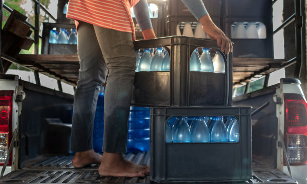 工人们把装在板条箱里的蓝色饮用水瓶子抬到一辆运输卡车的后面，在生产线里净化饮用水，准备出售。饮水厂，小本经营图片下载