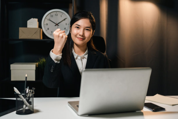 可爱的亚洲女商人晚上用笔记本电脑工作。漂亮的西装女坐在黑漆漆的办公室里加班到深夜。图片下载