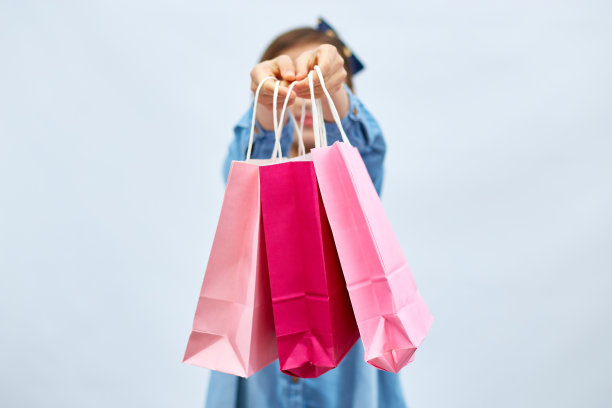 漂亮的小女孩穿着休闲的牛仔裙，手里拿着粉红色的购物袋图片下载