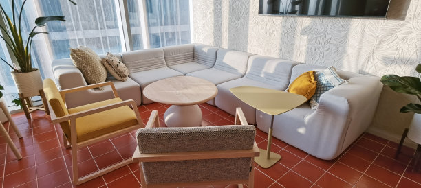 现代设计公司办公室休息区内部：沙发配枕头、扶手椅、茶几、咖啡桌，墙上有液晶显示屏，阳光充足图片下载