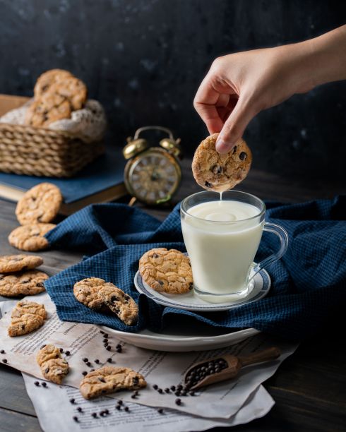 一个人的手把刚烤好的饼干倒进一杯乳白色的牛奶图片下载