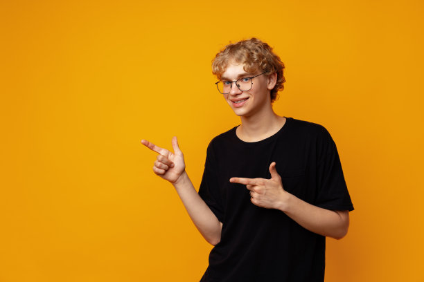 英俊的年轻人用手指指向黄色横幅背景上的复制空间图片下载