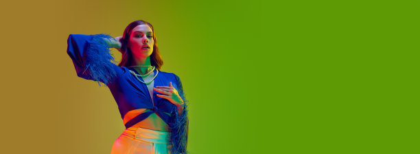 时尚模特，年轻的女孩，长波浪头发，穿着带有羽毛的衬衫，在霓虹灯的绿色渐变工作室背景下。模型铸造图片下载