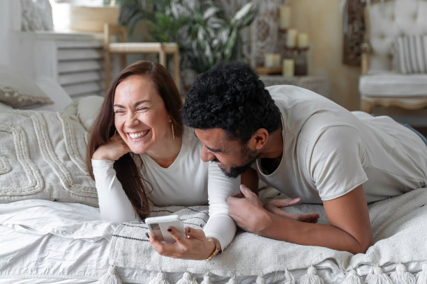 多种族美国夫妇一起躺在床上玩智能手机图片下载