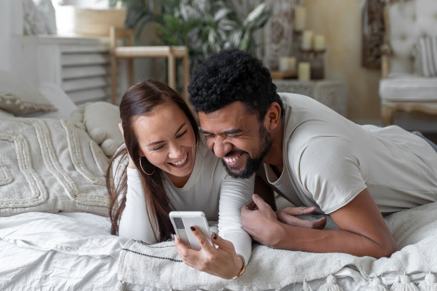 多种族美国夫妇一起躺在床上玩智能手机图片下载