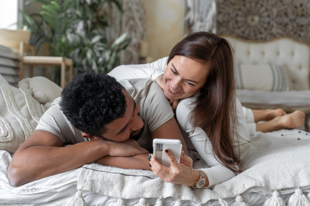 多种族美国夫妇一起躺在床上玩智能手机图片下载