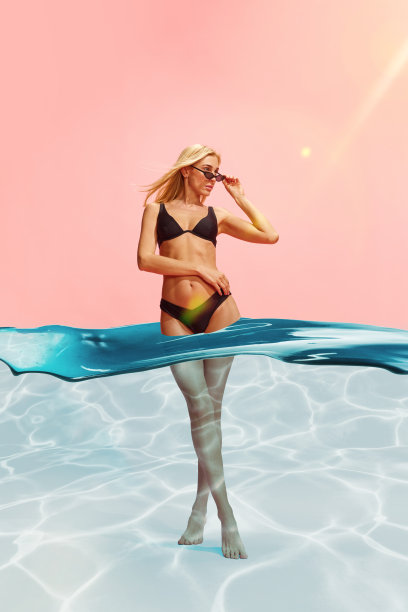 迷人的年轻女子，身材苗条，穿着时尚的黑色泳衣，粉红色的工作室背景与水的设计图片下载