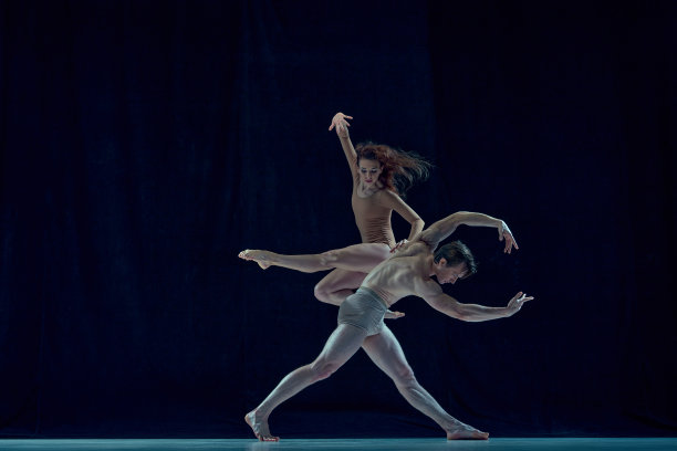 戏剧表演。年轻的男女，穿着米色衣服的芭蕾舞者，在蓝色的工作室背景下跳舞图片下载