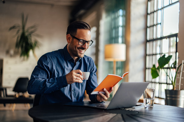 一个面带微笑的商人，端着一杯咖啡，读着他的练习本。图片下载