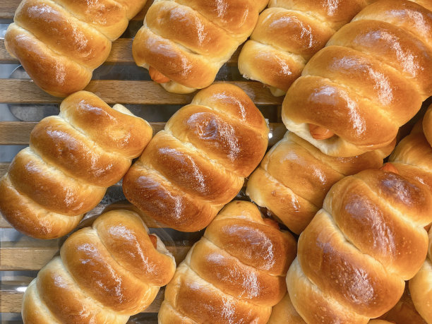 特写图片:一批热狗香肠包在面包卷里，堆放在面包店展示的木架子上，高架视图图片下载