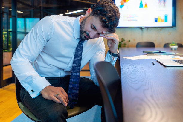 办公室里压力山大的商人。他穿着随意，一副心烦意乱的样子。他看起来很不舒服，可能还有头痛。图片下载