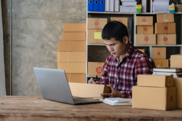 年轻的亚洲中小企业商人在仓库，家庭办公室，独立的快递公司工作，用笔记本电脑检查客户地址。图片下载