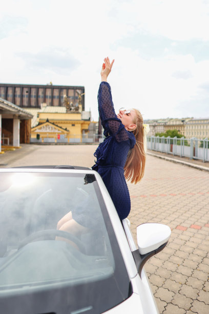 年轻迷人的金发女郎双手高举坐在敞篷车里图片下载