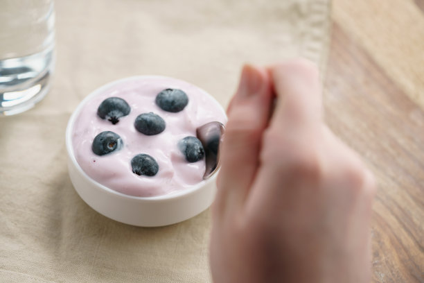 一个十几岁的女孩用手吃着有机蓝莓酸奶图片下载