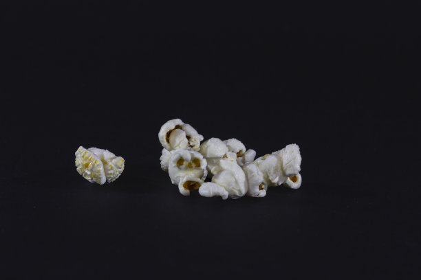 工作室拍摄的孤立的爆米花在一个黑色的背景前，咸和甜，黄油味。它是一种加热后会爆开的玉米仁，在电影院里被当作垃圾食品吃。图片下载