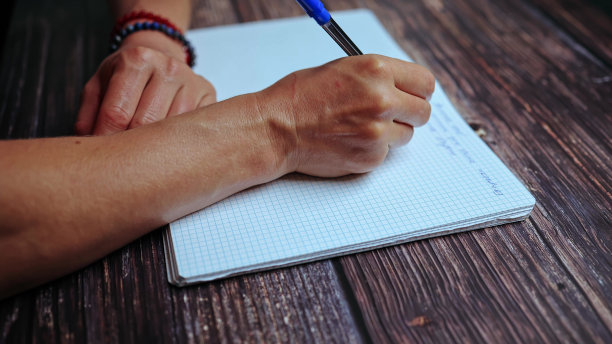 这个学生正在做作业，在笔记本上记笔记。木桌上，一个女人的手拿着一支笔在笔记本上写字。图片下载