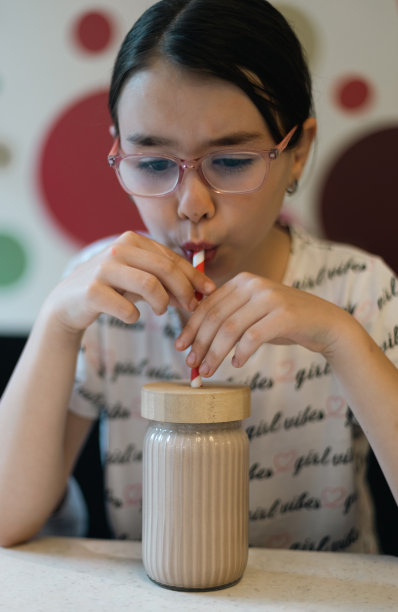 一个单身白人女孩用玻璃杯喝奶昔的画像。图片下载