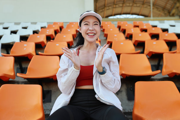 图为快乐而兴奋的亚洲年轻女体育迷，她坐在体育场的空座位中，为获胜的球队欢呼并鼓掌观看比赛图片下载