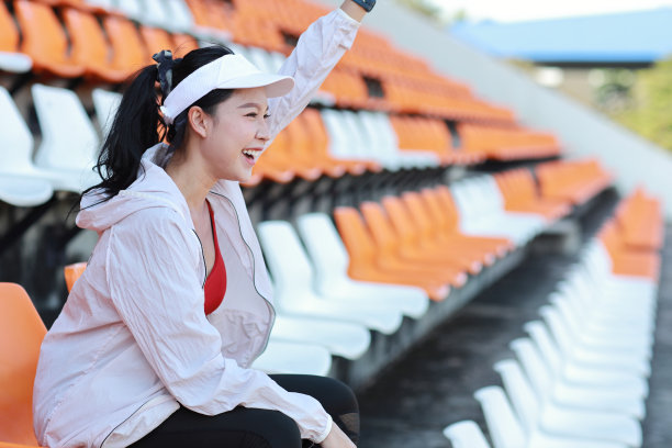 图为快乐而激动的年轻亚洲女体育迷，她坐在体育场的一排排空座位中，用拳头欢呼和观看比赛，为获胜的球队庆祝图片下载