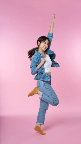 年轻的亚洲女子戴着耳机跳舞，听着粉色背景下智能手机拍摄的音乐图片下载