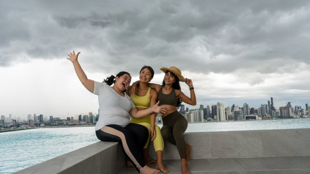 朋友们在摩天大楼屋顶的游泳池里玩得很开心，做完瑜伽后在游泳池里对着现代摩天大楼冥想自拍。年轻女孩在屋顶公寓外面做运动图片下载
