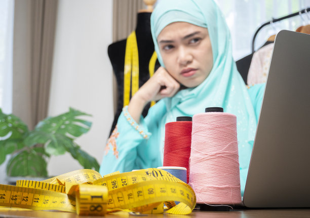 年轻的穆斯林女售货员在店里检查服装细节，在电脑上写数据，表情严肃。图片下载