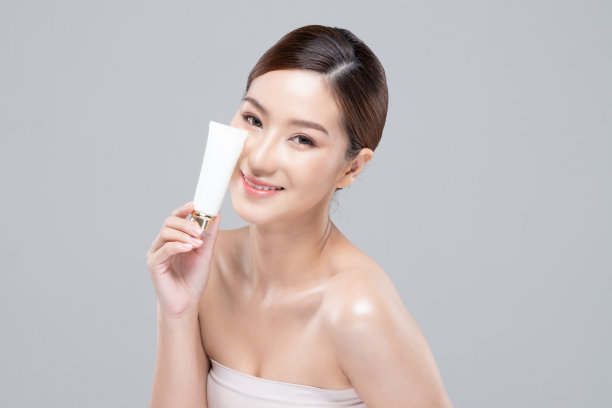 美丽年轻的亚洲女子手持奢华的白色清洁管微笑，感觉如此快乐和愉快，健康清洁和新鲜的皮肤，隔离在灰色的背景，美容化妆品水疗和治疗概念图片下载