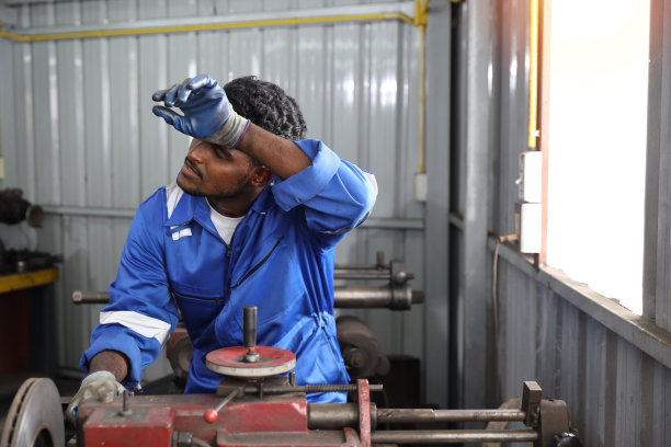 疲惫的热工和热工穿着制服，在车库边擦汗边用金属车床抛光汽车盘式制动器。维修汽车车辆零件的概念图片下载