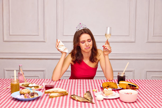 年轻漂亮的女孩庆祝生日，坐在餐桌旁，喝着香槟，哭着。变老。餐桌上的美味小吃图片下载