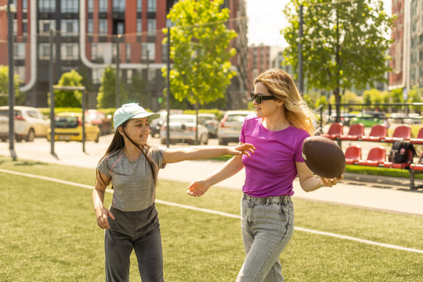 母亲，女儿，椭圆形棕色皮革橄榄球在公园里玩美式橄榄球。家庭和孩子，自然的概念。图片下载