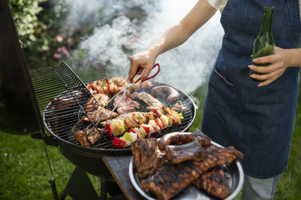 妇女在烤架上烤肉和蔬菜。图片下载
