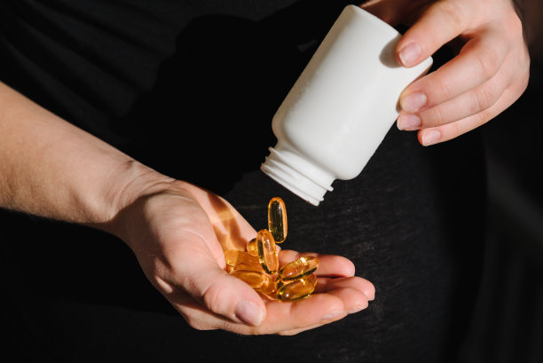 ω- 3。孕妇每天服用维生素。特写照片的女性手拿补品或维生素与一个白色的瓶子。放文字的地方。妊娠、治疗、医药保健理念。图片下载