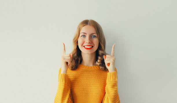 幸福的肖像激动的微笑的年轻女子指着她的手指在白色的背景，空白的复制空间图片下载